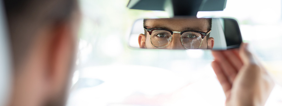 Chico con gafas mirándose por el espejo del retrovisor en el coche.